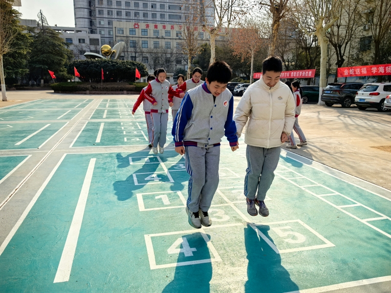 在济南五中的课间，跳格子、打羽毛球、踢毽子，这些经典游戏重焕生机，同学们再拾童年乐趣，在画好的格子上，蹦蹦跳跳，在简单的游戏中释放活力，享受运动的乐趣，尽享纯粹欢乐的课间时光。